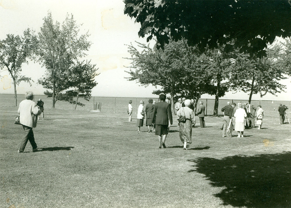 Black and white photograph of a group of people walking across a greenspace towards a lake