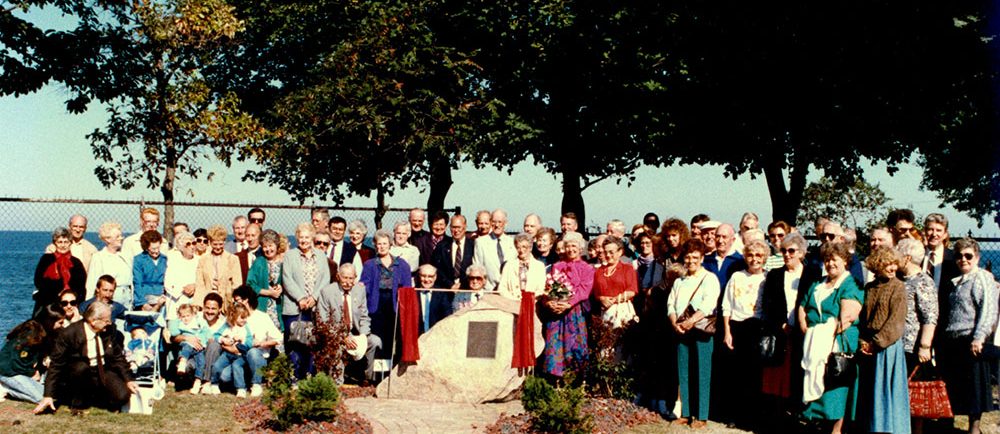 Colour photograph of a large group of people gathered around a stone with a plaque on it