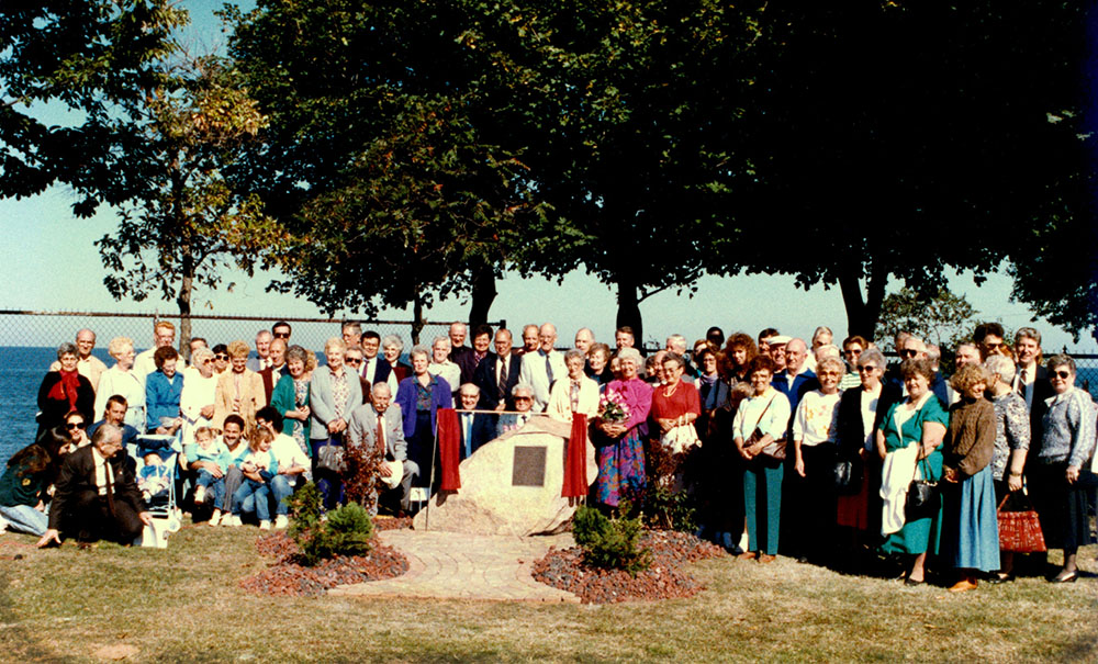 Colour photograph of a large group of people gathered around a stone with a plaque on it