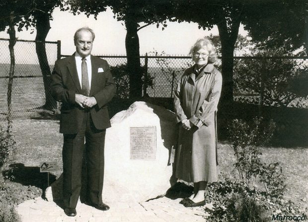 Black and white photograph of a man and a woman standing with a stone with a plaque on it