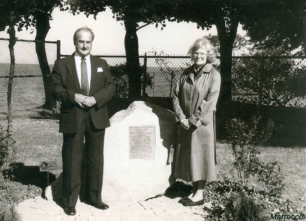 Black and white photograph of a man and a woman standing with a stone with a plaque on it