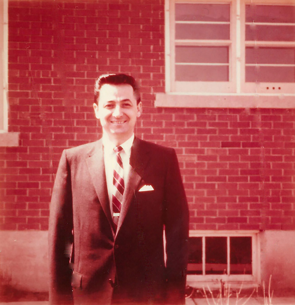 faded colour photograph of a man in a suit in front of a house