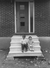 Photo noir et blanc de deux enfants sur les marches d’une maison.