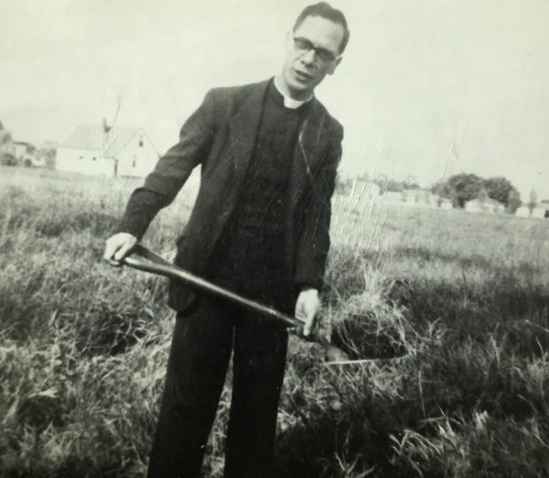 Photograph of a priest holding a shovel digging in a field
