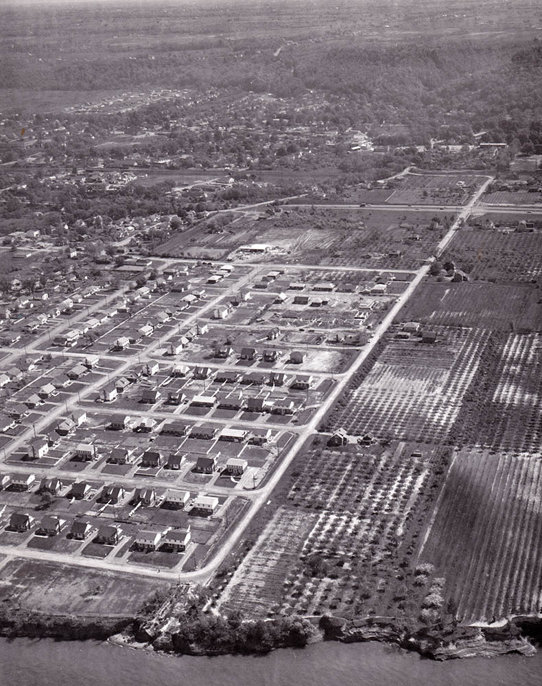 Black and white photograph of an aerial view of Grimsby showing rows of single family dwellings with large yards near the lake front.