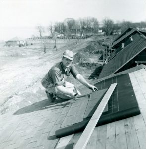 Black and white photograph of a man shingling a roof