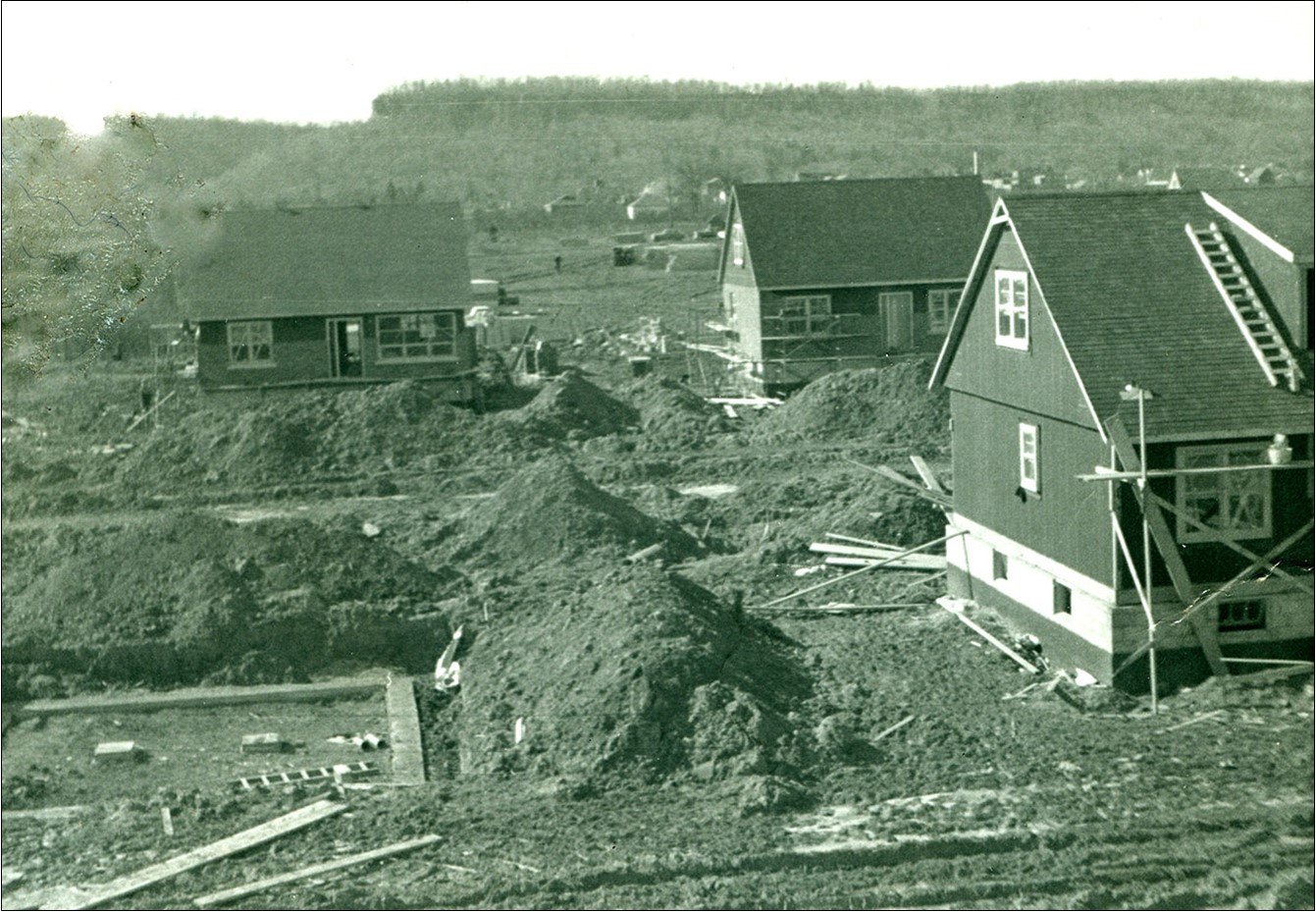 Black and white photograph of homes under construction. Piles of dirt are all around