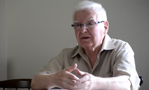 colour photograph of a man in a tan shirt sitting to the right of the screen