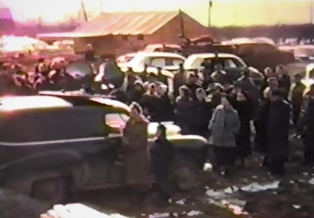 Older colour photograph of a group of people standing around some cars