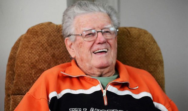 Colour photograph of a man in an orange shirt sitting in a chair laughing