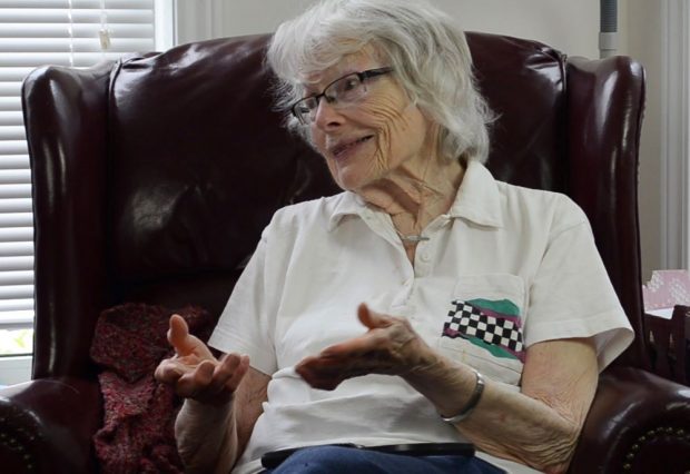 colour photograph of a woman sitting a chair facing left and using her hands to explain what she is talking about