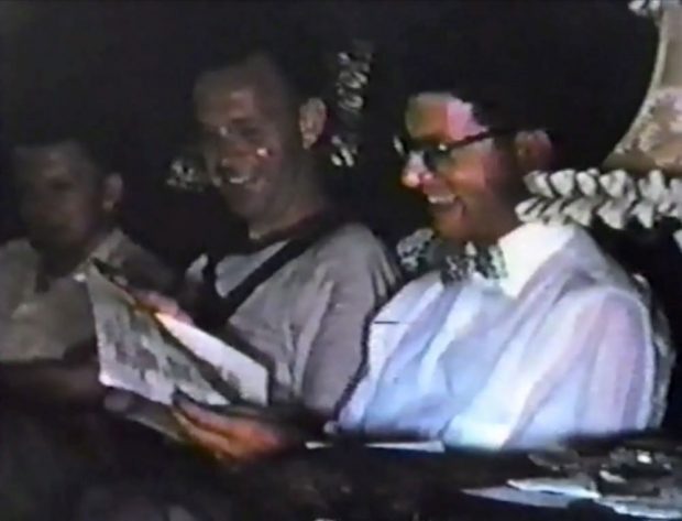 older colour photograph of two men reading papers and smiling