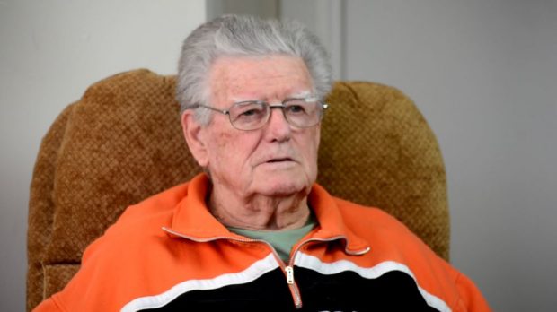 colour photograph of a man in an orange shirt in the centre of the photograph