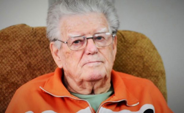 colour photograph of a man in an orange shirt in the centre of the photograph