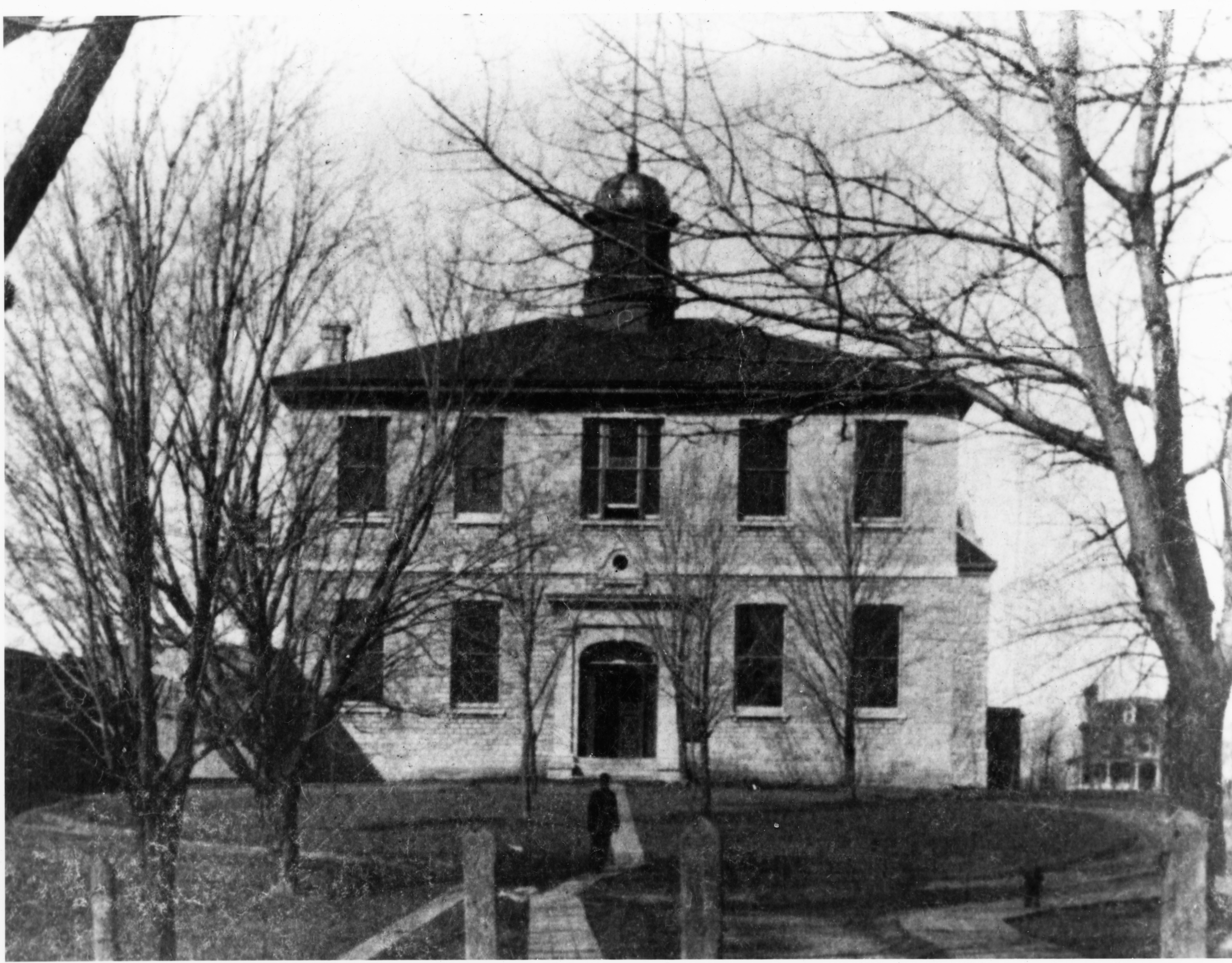 Photo de l'édifice médical de Queen vers 1880 avec des arbres et un individu devant.