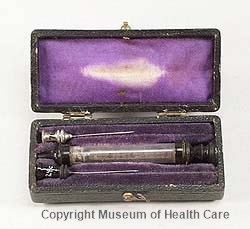 Photograph of hypodermic syringe case containing a glass hypodermic syringe and two metal needles circa 1870