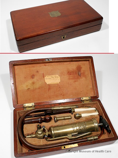 Photograph of a stomach and enema pump with metal syringe and tubing and accessories in a fabric-lined wooden case