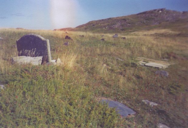 A colour photograph of a graveyard on a grassy hill.