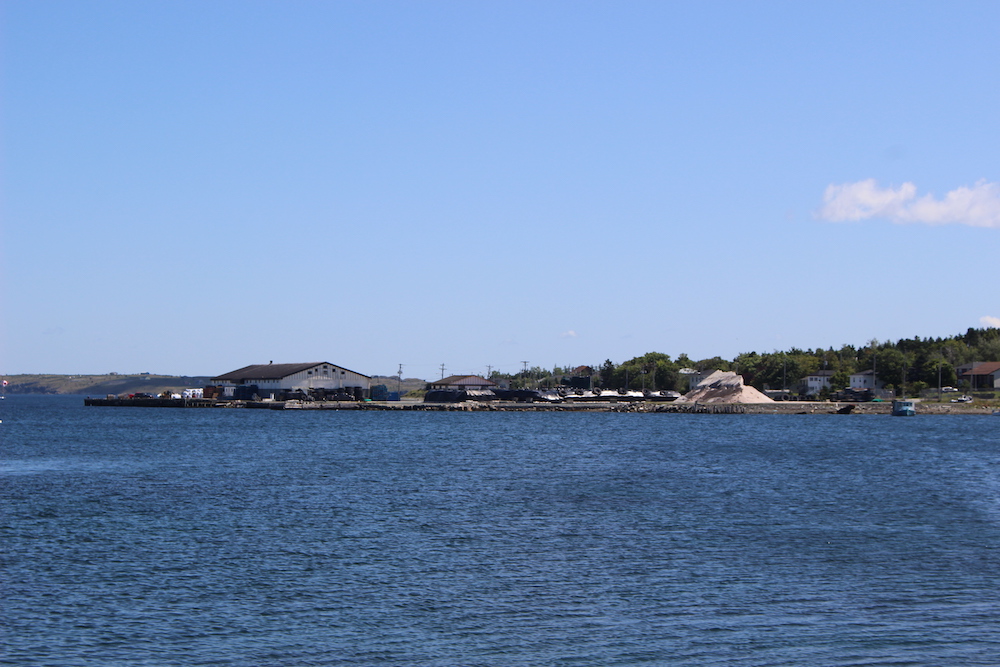 A view across the water, showing various mercantile buildings and a large pile of road salt.