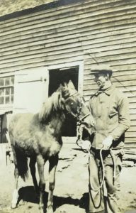 Photographie en noir et blanc d’un jeune homme posant à côté d’un cheval.