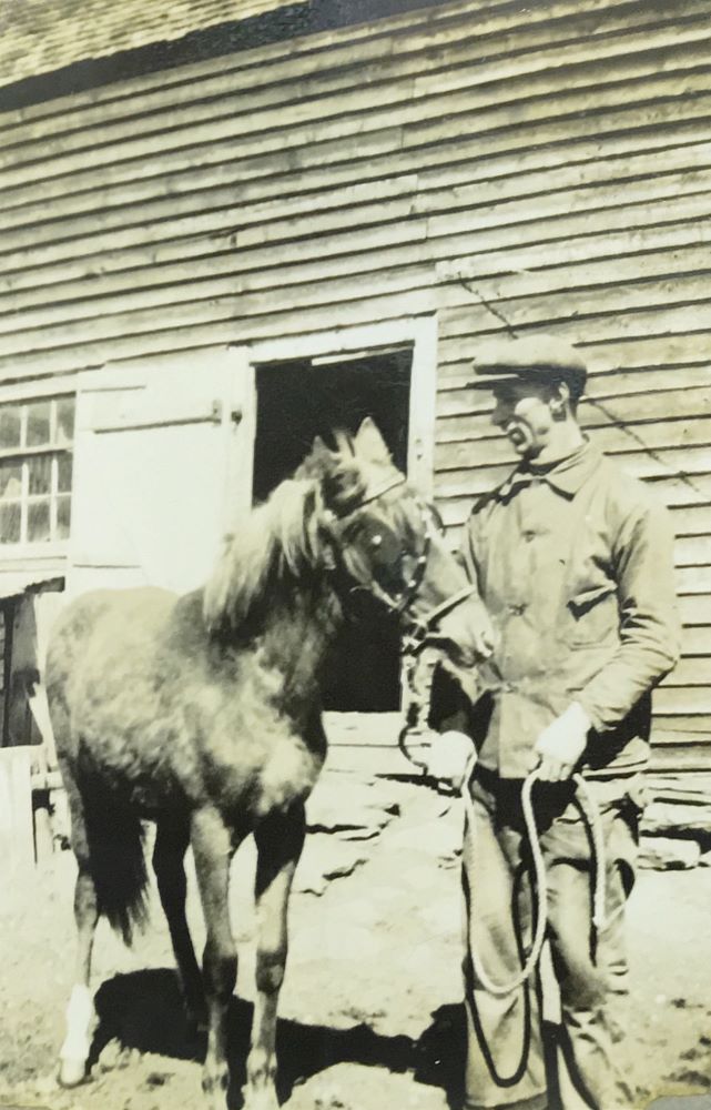 Black and white photograph of a young man posing beside a horse.