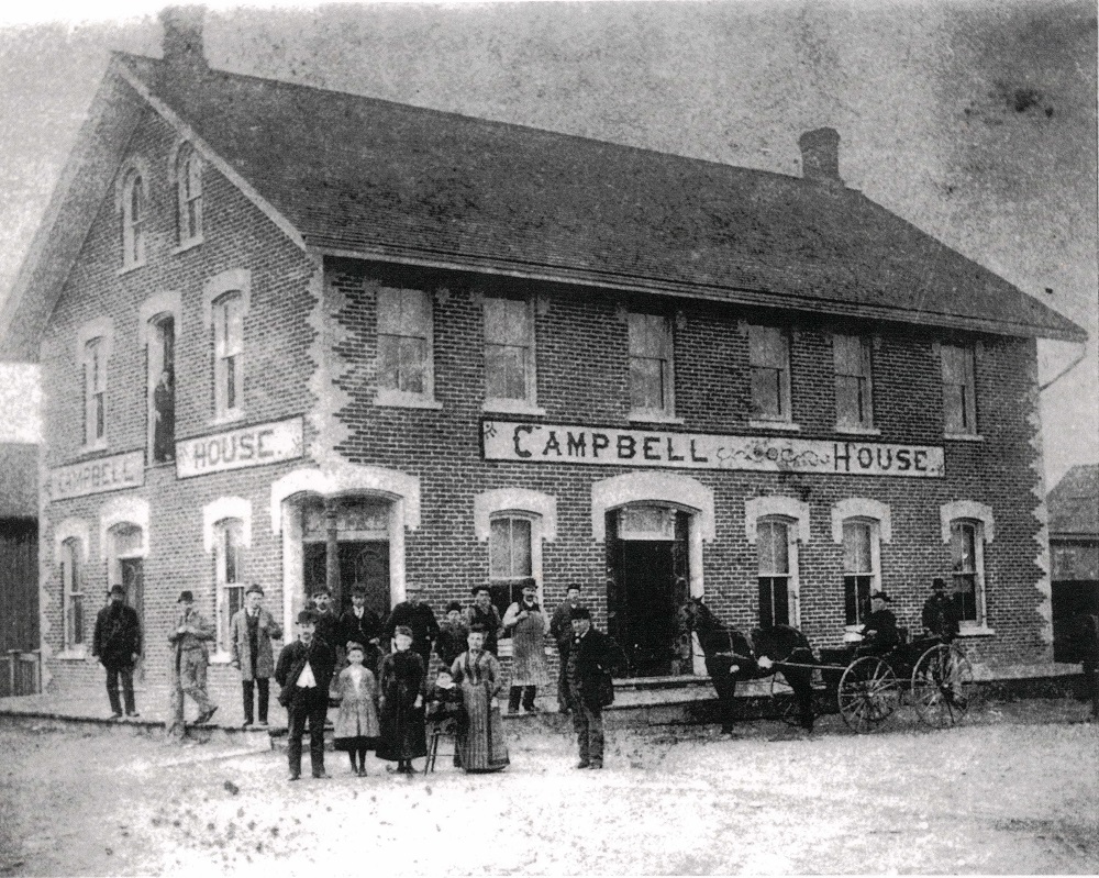Black-and-white image of brick building with people gathered on street in foreground