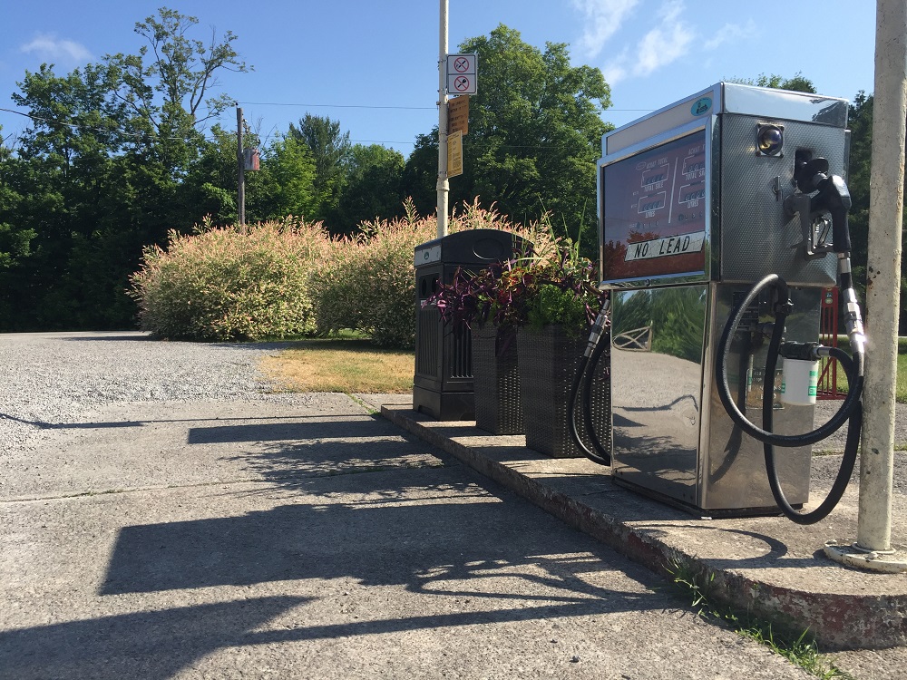Colour image of gas pump, planters, and garbage receptacle with shrubs and trees in background
