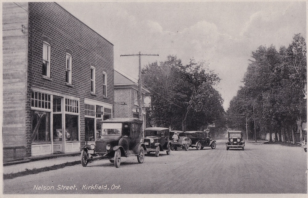 Black-and-white image of vintage cars parked in front of building with trees in background