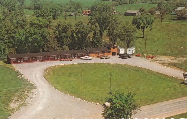 Colour image of long building, vintage cars, lawn, and highway taken from the air