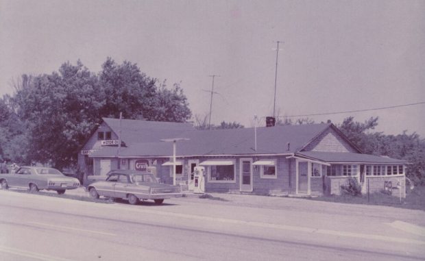 Colour photograph of building with cars and gas pumps in the foreground