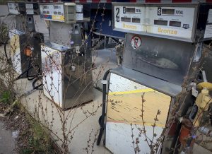 Colour image of three gas pumps with weeds growing in foreground