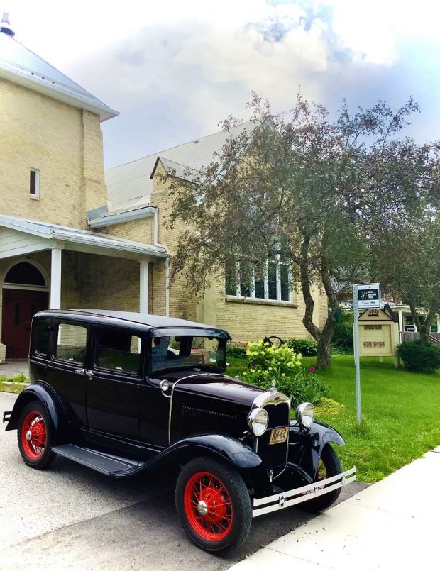 Vintage vehicle in front of building with tree in foreground and sky in background