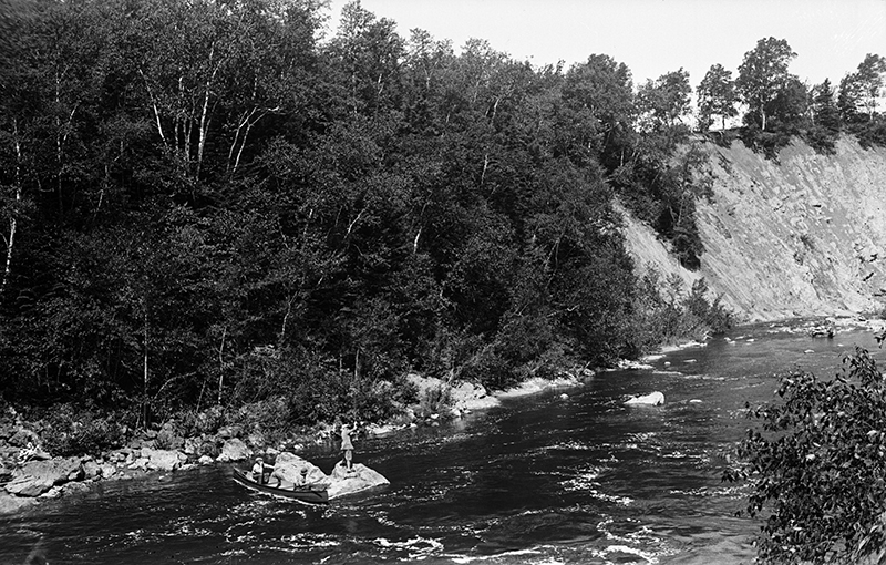 View from the steep banks of the river rising sharply of the swirling pools where a fisherman is fishing standing on a rock.