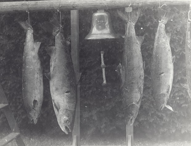 Silver print of four fish suspend on the bell in the front of Estevan Lodge
