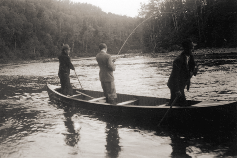 Lord Tweedsmuir fishing standing in a canoe on the Metis River