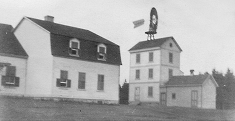 Silver print of the back of Estevan Lodge showing an adjacent building toppped by a eolian