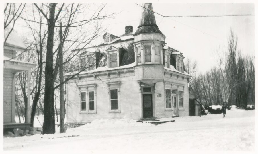 Black and white winter photograph of the J A Rousseau bank a building of Second Empire style with gable dormer and turrets.