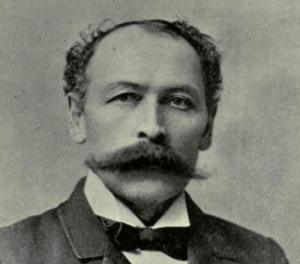 Photographie portait en noir et blanc de Jeffrey Alexandre Rousseau portant la moustache et habillé d’un complet avec nœud papillon.