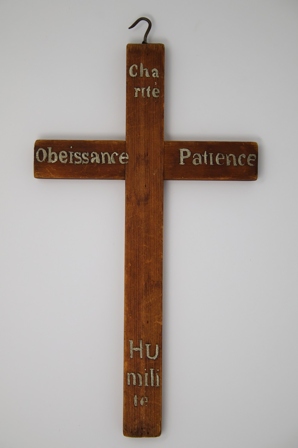 Photograph of a brown wooden cross where the words “charity” “obedience” “patience” and “humility” appear in golden characters on each end.