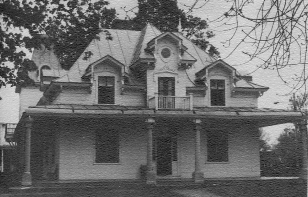 Black and white front view photograph of John Jones Ross’s house a charming villa surrounded by a covered porch with columns and a four gabled roof with symmetrical openings.