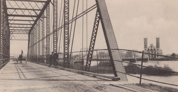 Black and white photograph of the Sainte-Anne-de-la-Pérade’s iron bridge built after the 1894 scree on which stand two men and a horse-drawn carriage.