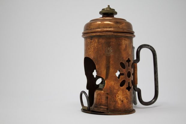 Photograph of a copper kerosene lamp with an ornament carved into a rosette shape.