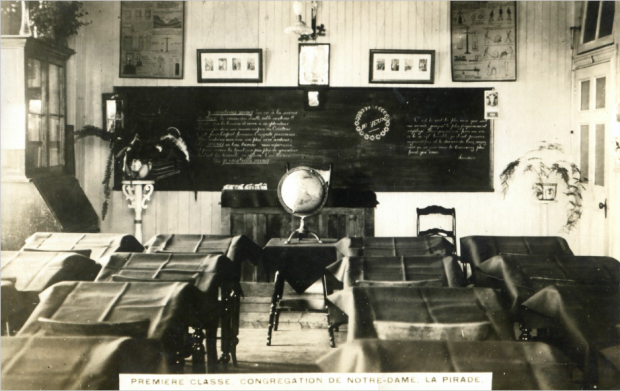 Black and white photograph of a Sainte-Anne’s convent class with a blackboard a terrestrial globe and desks covered with sheets.