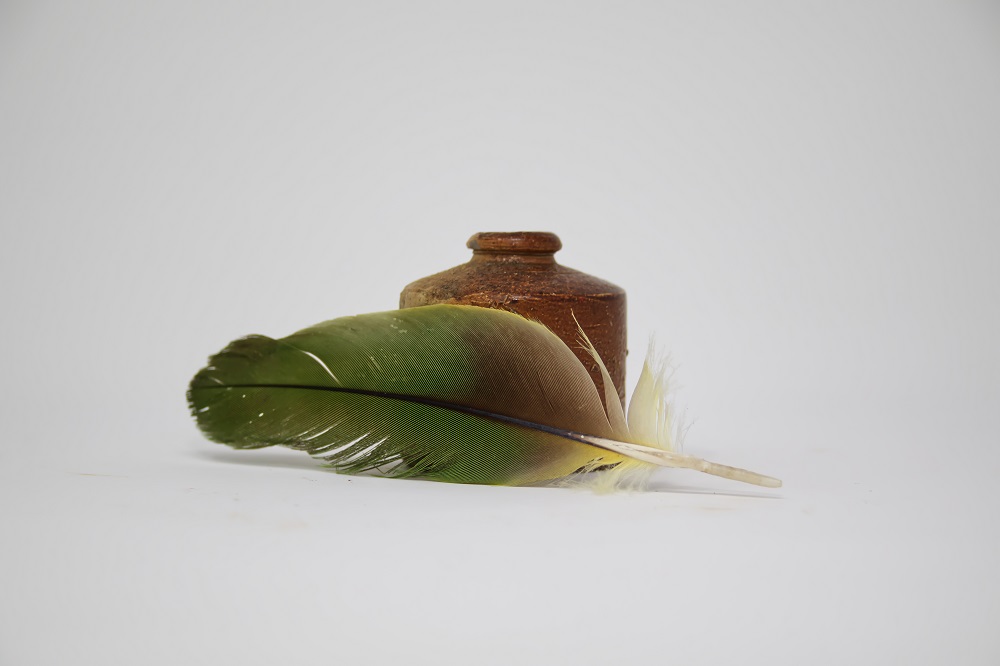 Photograph of a quill and a cylindrical inkwell made of ceramic and sandstone.