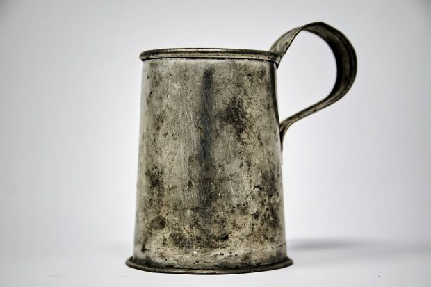 Photograph of a worn metal and iron cup with a handle.
