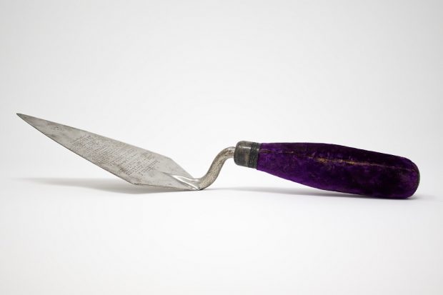 Metal trowel with its handle covered with purple velvet on which is carved an inscription.