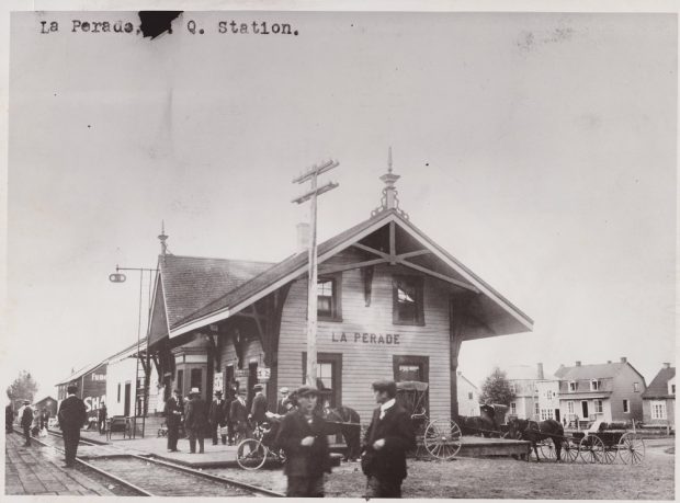 Black and white photograph of Sainte-Anne-de-la-Pérade railway station where travellers and a horse-drawn carriage are gathered.
