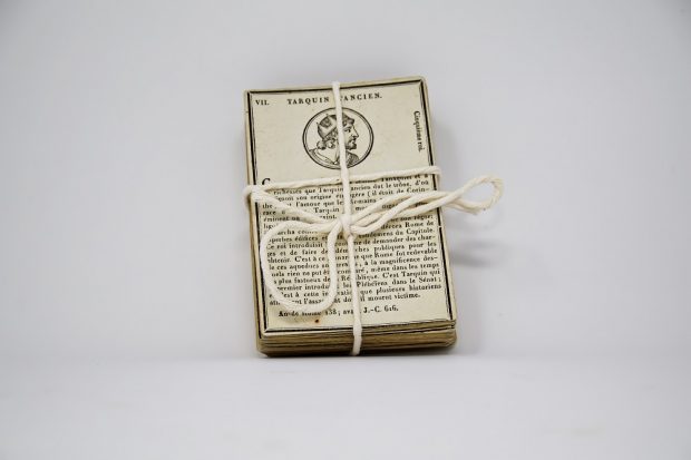 Tied deck of cards made from cardboard from the 18th century. The card on top of the deck shows a drawing of Tarquin l’Ancien with a brief biography.