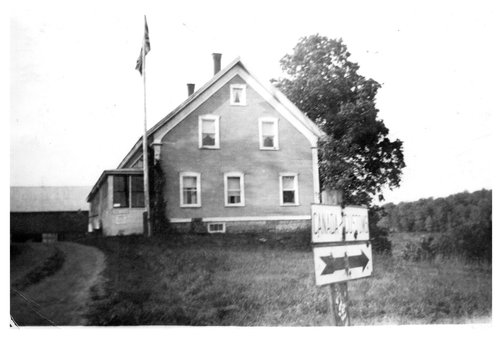 Side view of the combined East Pinnacle house and customs post with: a flagpole in front, and an arrow under the words Canada and US to indicate the location of the border.