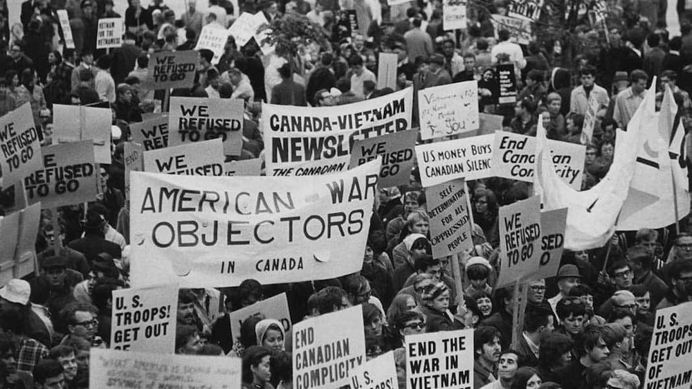 Anti-Vietnam war protesters. Their signs read: End the War in Vietnam, End Canadian Complicity, American War Objectors in Canada.